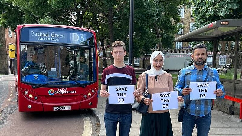 Lib Dem activists Dominic Buxton, Rabina Khan and Mahbub Alam hold signs reading Save the D3 bus in front of the D3 bus on Wapping Lane